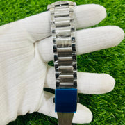 Silver watch with blue face held by a gloved hand on grass