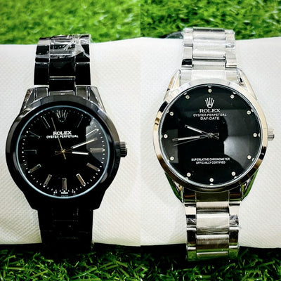 Two Rolex watches, one black and one silver, on a white surface with grass in the background.