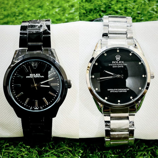 Two Rolex watches, one black and one silver, on a white surface with grass in the background.